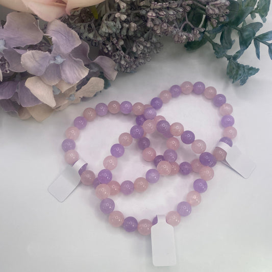 Pink and Purple beaded Rose Quartz & Amethyst Bracelet on a white surface with flowers in the background